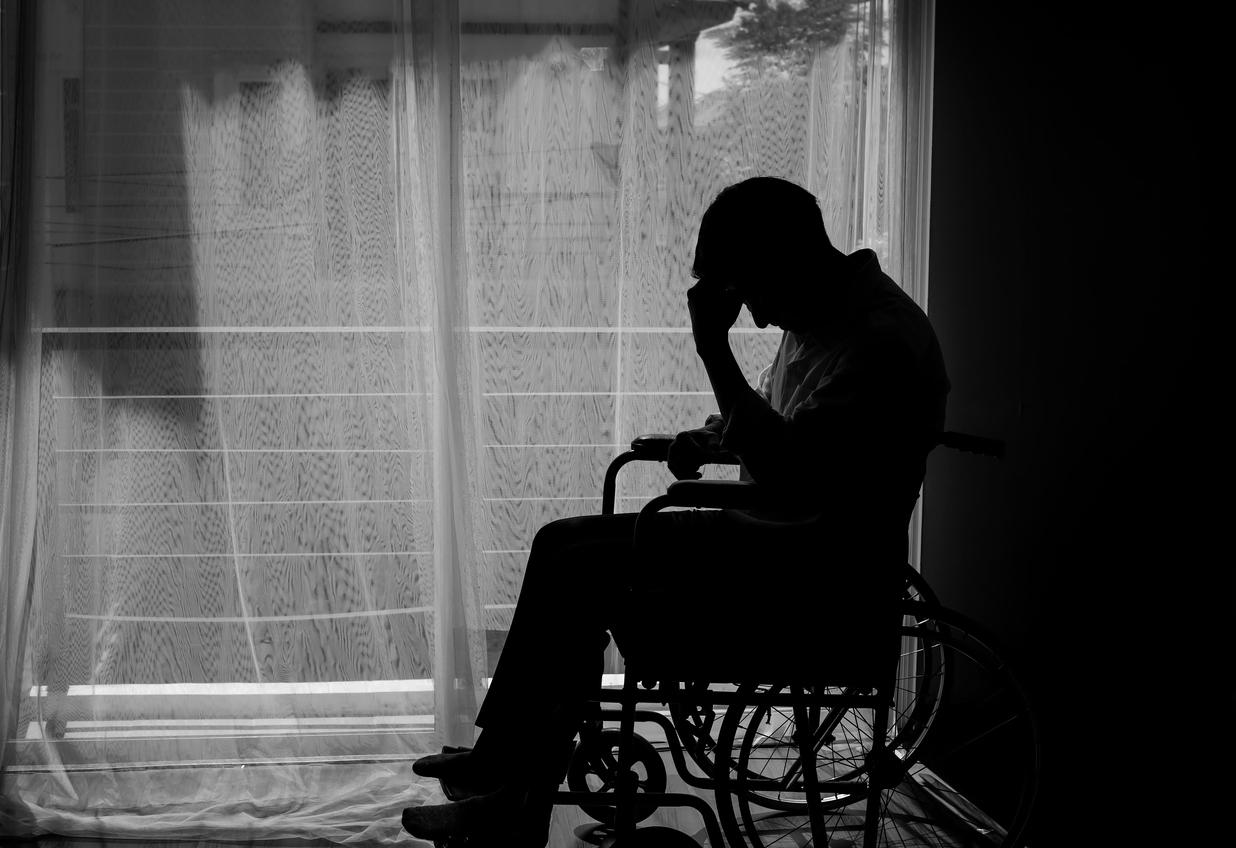 Black and white photo of man in wheelchair looking hopeless and he leans his head into his hand